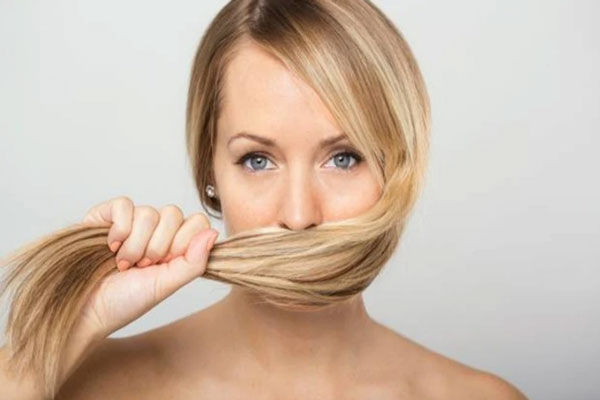 Tricofagia - Mujer rubia de ojos azules se tapa la boca con el largo de su cabello 