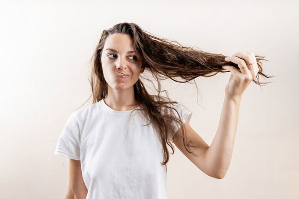 Tricotilomanía - Mujer hace una mueca tras sostener su cabello reseco y deshidratado