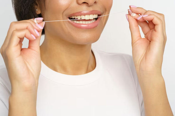 Mujer de piel morena usa hilo dental para eliminar los restos de comida de su boca 