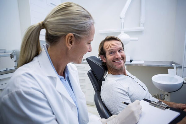 Caries y calvicie - Dentista toma nota de los datos de un paciente para proceder a realizarle una limpieza dental en su consultorio 