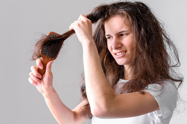 Mujer con cabello extremadamente reseco intenta deshacer nudos en las puntas de su melena 