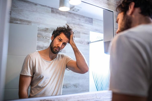 Fases del crecimiento del pelo - Hombre se para frente al espejo visiblemente preocupado por su salud capilar