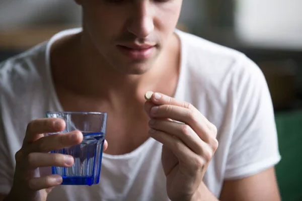 Joven toma analgésicos con un vaso de agua para aliviar el dolor