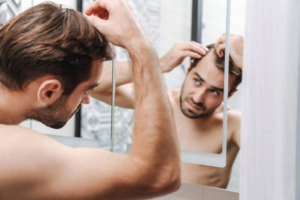Alopecia en jóvenes - Hombre joven se muestra preocupado frente al espejo ante el avance de las entradas en la sien