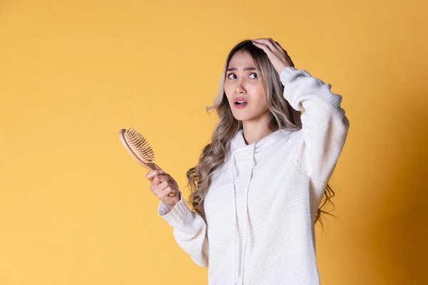 Alopecia en jóvenes - Mujer de cabello teñido se toca la cabeza con angustia ante pérdida sostenida del pelo