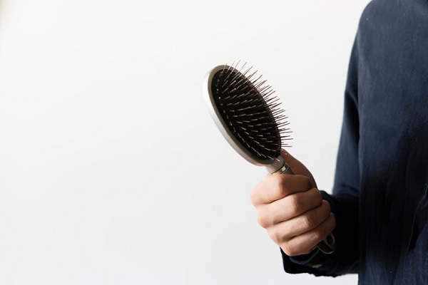 alopecia juvenil - Joven de camisa azul marina sostiene un cepillo con la mano para cuidar su cabello