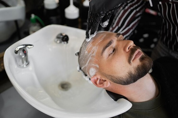 Barbero lavando el cabello de un hombre con un champú suave de pH neutro, para cuidar y fortalecer los folículos pilosos implantados