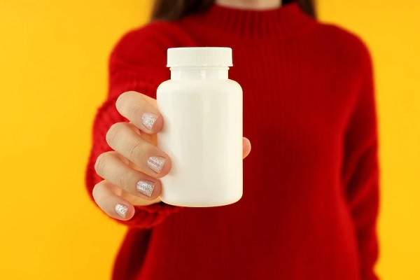 Espironolactona - Mujer con suéter rojo sosteniendo un recipiente de pastillas