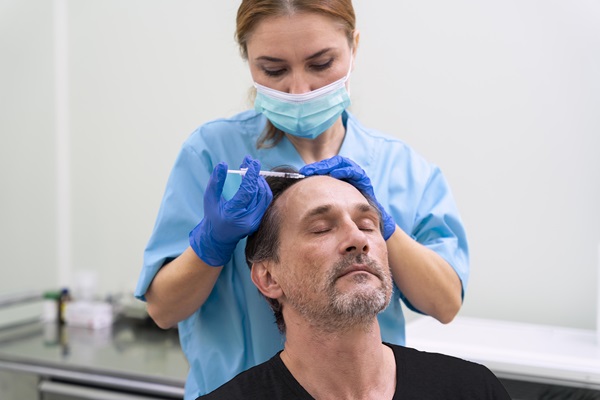 Dermatólogo en el injerto capilar - Dermatóloga realizando un tratamiento capilar a un paciente masculino, para fortalecer y estimular el crecimiento del cabello