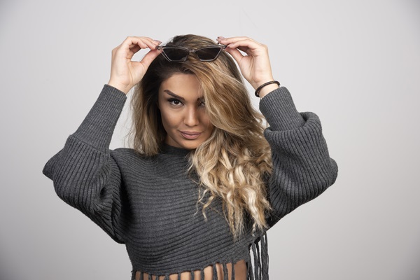 Mujer con tinte en el pelo de color rubio posando mientras sostiene unos lentes en su cabeza