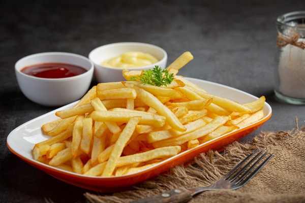 Imagen de un plato de papas fritas junto a varias salsas, lo cual es perjudicial para la salud debido al exceso de grasa