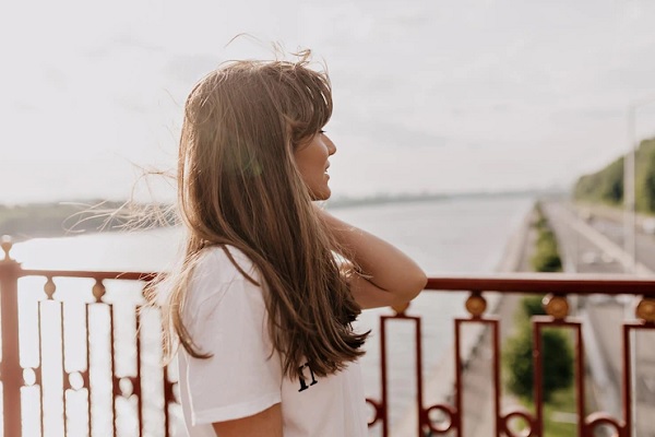 El sol daña el cabello - Mujer posando mirando al horizonte, mientras los rayos UV impactan directamente en su cabello