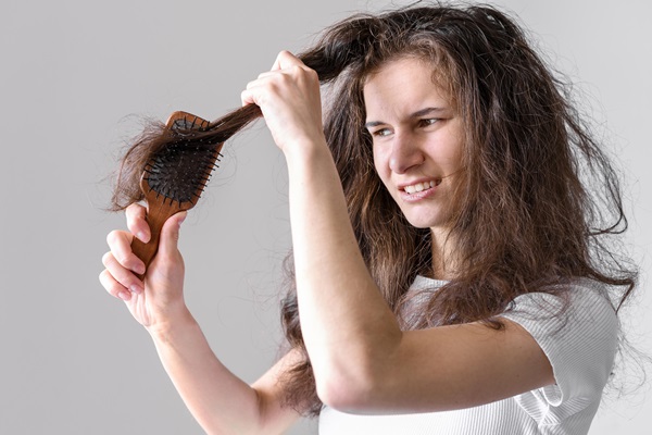 Mujer abrumada intentando cepillar su pelo con frizz, debido al gran daño que poseen las hebras capilares por la falta de hidratación