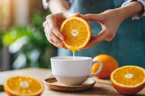 Cabello sano desde adentro - Mujer exprimiendo naranjas en una taza, ya que el jugo de naranja es una buena fuente de vitamina C