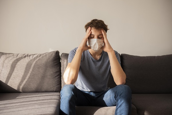 Hombre sentado sujetando su cabeza y utilizando una mascarilla para no propagar la enfermedad que padece