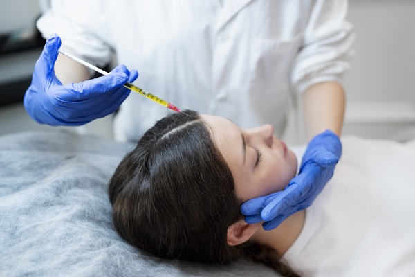Médico especialista aplicando una inyección en el cuero cabelludo de una paciente femenina, para revitalizar el cabello