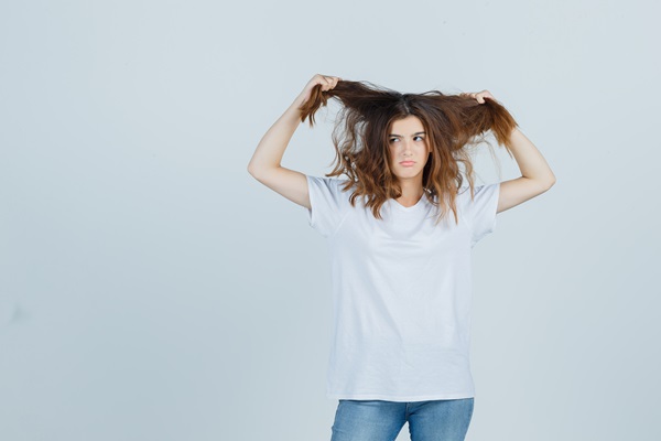 El sol daña el cabello - Mujer triste sosteniendo su cabello, el cual se encuentra enredado y opaco debido a la deshidratación capilar