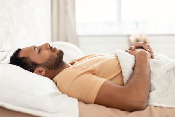 Hombre moreno duerme boca arriba con las manos sobre el abdomen