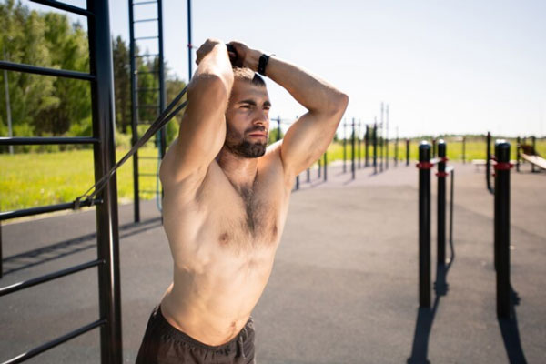 Deportes tras un injerto capilar - Joven sin camisa realiza ejercicios con ligas para tonificar sus brazos