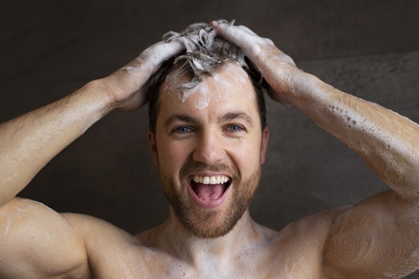 Caspa en los hombres - Hombre joven sonriente lava su cabello con champú