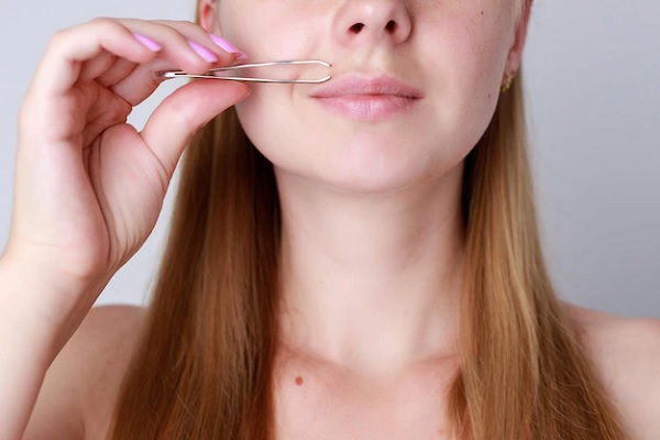 Hirsutismo hormonal - Mujer rubia recurre al uso de una pinza para remover vellos faciales