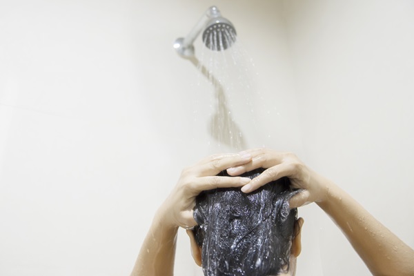 Mujer debajo de la ducha enjuaga su cabello con abundante agua para retirar el champú