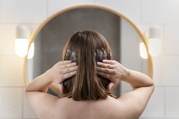 Caída del cabello - Mujer aplicando una mascarilla hidratante en su cabello frente a un espejo