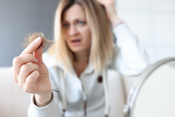 Alopecia en la menopausia - Mujer rubia con mechón de pelo en mano manifiesta preocupación por la caída de su cabello