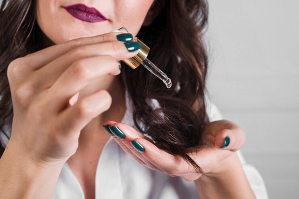 Mujer de labios pintados aplica un serum hidratante en las puntas de su cabello