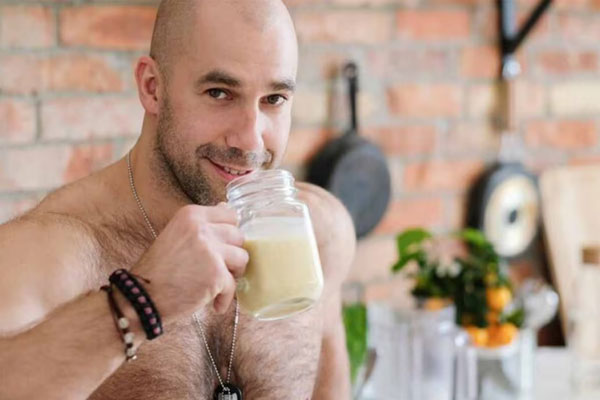 Batidos de proteína y calvicie - Hombre calvo y musculoso se toma un batido verde en la cocina