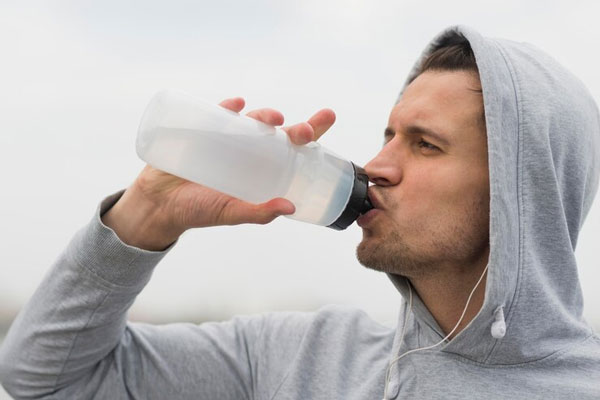 Primer plano de un hombre con suéter bebiendo agua