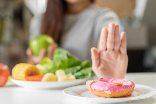 Joven con manzana verde usa su mano para rechazar un plato de dona 