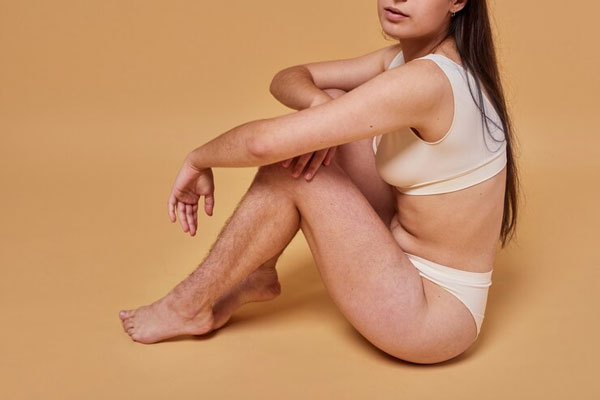 Hirsutismo hormonal - Joven en ropa interior con exceso de vello en las piernas posa frente a la cámara