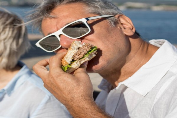alimentos que causan la caída del cabello - hombre con problemas de alopecia en las entradas y la línea del cabello comiéndose una hamburguesa