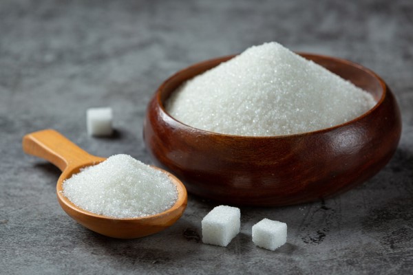 alimentos que causan la caída del cabello - Azúcar en un tazón de madera sobre una superficie oscura