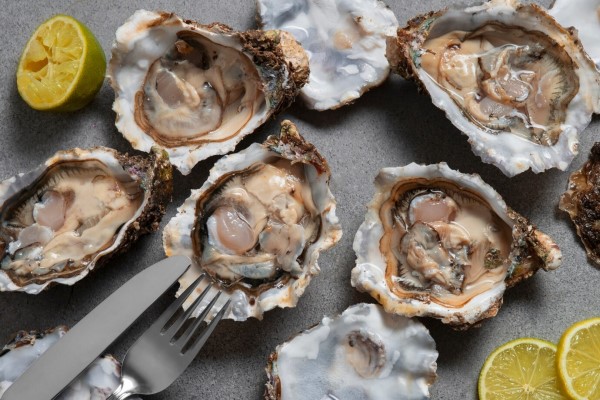 alimentos que causan la caída del cabello - ostras crudas con limón, un cuchillo y tenedor