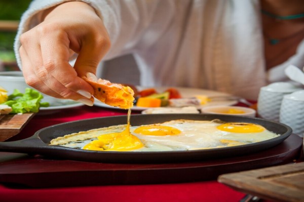 alimentos que causan la caída del cabello - mujer en albornoz sentada en la mesa desayunando huevo frito