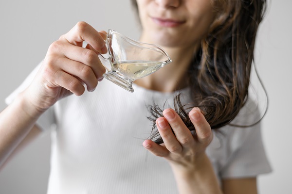 Mujer joven sostiene una taza para aplicar un aceite natural en el cabello