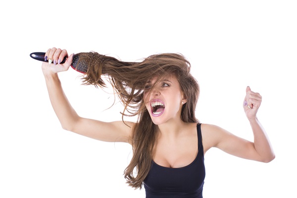 Hair slugging - Mujer joven con cara de frustración usa un cepillo para desenredar su cabello