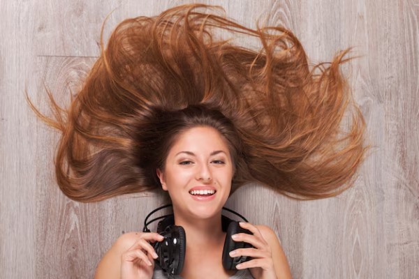 Beneficios del aloe vera en el pelo - mujer tumbada en el suelo con unos auriculares en el cuello y su melena extendida por el piso