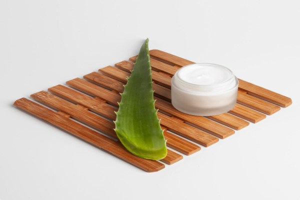 Beneficios del aloe vera en el pelo - hoja aloe vera cortada al lado de un bote de mascarilla capilar sobre una esterilla de madera