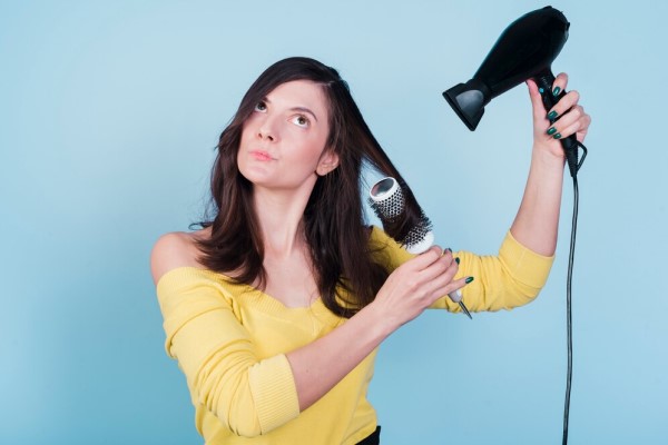 Peinados que debes evitar - mujer realizándose un peinado con herramientas de calor