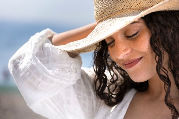 mujer sonriente bajo el sol con un sombrero para proteger el cabello de los rayos UV