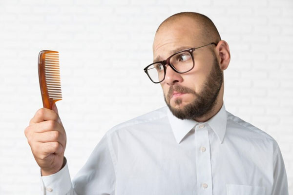 Sistema de integración capilar - Hombre con alopecia mira su peine con tristeza tras enfrentar una gran pérdida de cabello