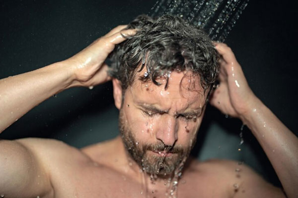 Hombre lava y aclara su cabello con abundante agua bajo la ducha