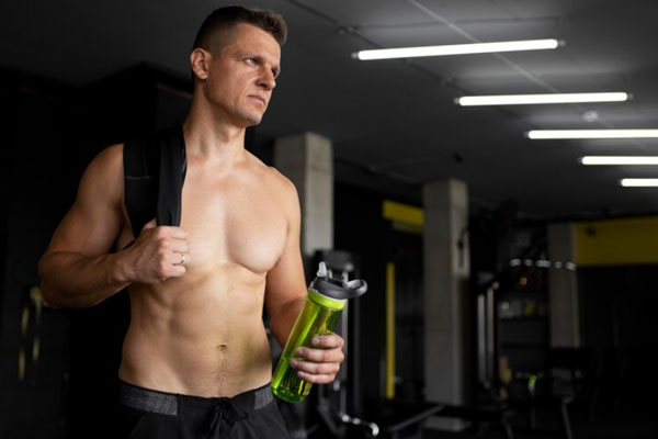 Hombre atlético sin camisa y con botella de agua en mano concluye su rutina de entrenamiento en el gimnasio