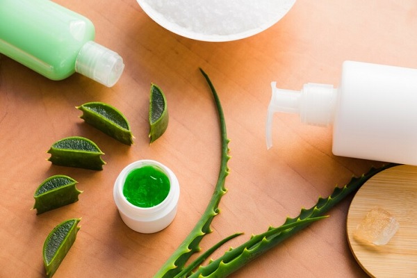 beneficios del aloe vera en el pelo - hojas de aloe vera al lado de productos y envases para tratamientos capilares