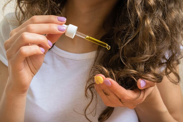 Joven de pelo rizado usa aceite de argán para combatir el frizz y las puntas abiertas 