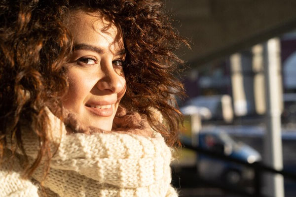 Cabello en invierno - Mujer con cabello rizado intenta controlar el frizz y el encrespamiento en temporada de frío 