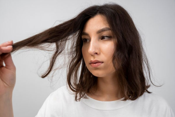 Mujer con cabello maltratado y opaco observa con detenimiento las puntas de su melena 